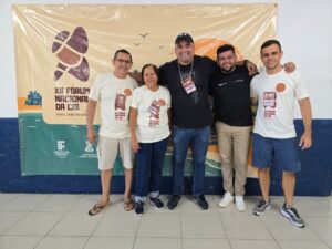 Quatro homens e uma mulher com banner ao fundo nas cores amarelo e verde com os dizeres décimo segundo fórum nacional das CIS